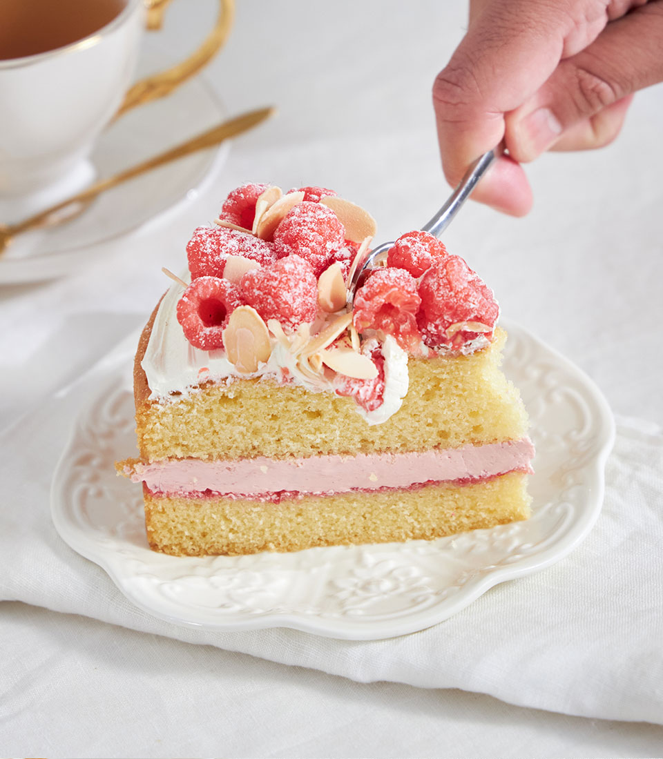 Raspberry and almond cake slice with cream and fresh berries on floral plate, tea service