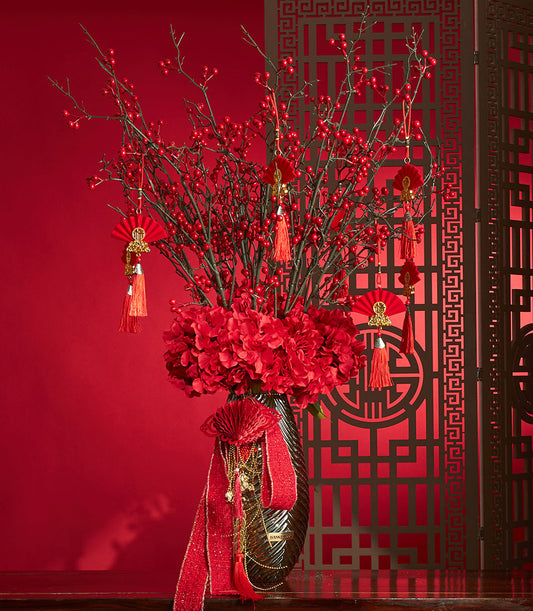 Basketeer's festive Chinese New Year gift: red berry branches and hydrangea in a vase, adorned with tassels and a wide, shimmering red ribbon.