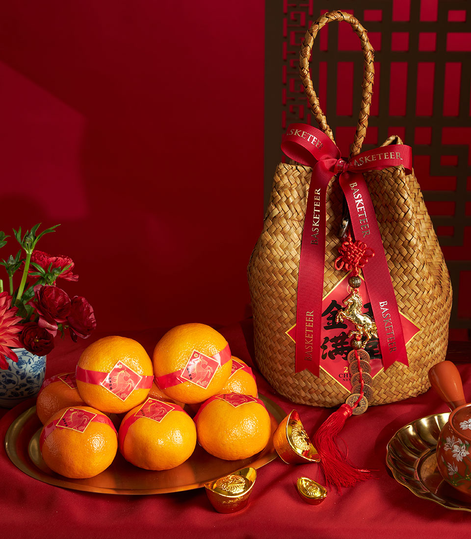 Prosperity mandarin orange gift bag with woven basket, red ribbon, Chinese New Year fortune charms, and fresh red flowers