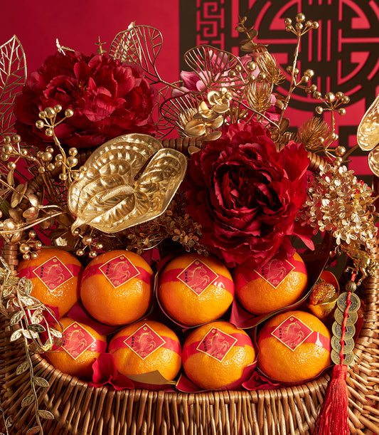 Woven wicker luxury basket with bright mandarin oranges, red ribbons, deep red peonies, gold leaves, and festive Chinese New