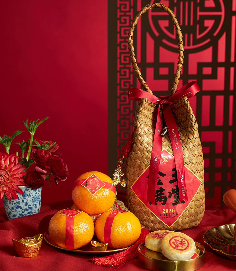 Chinese New Year mandarin orange gift basket with woven straw, red satin ribbon, gold ingots, and festive red flowers