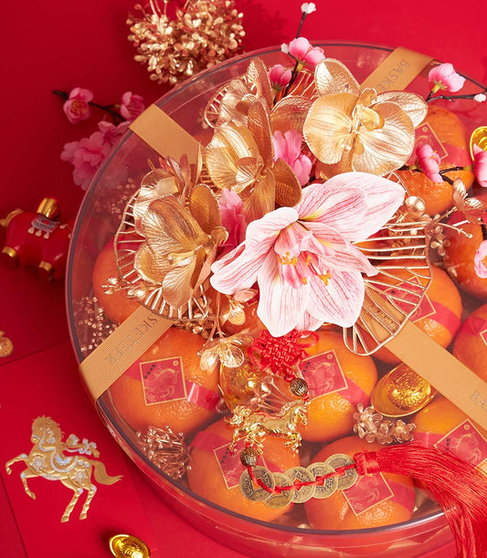Festive mandarin orange gift basket with gold orchids, pink amaryllis, and red silk wrapping for Chinese New Year