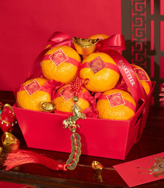 Vibrant red gift basket filled with individually wrapped mandarin oranges, gold horse charms, and lucky coins for Chinese