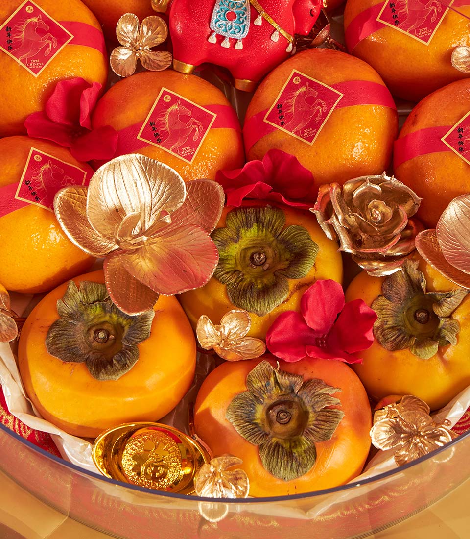 Festive mandarin orange and persimmon gift tray with red ribbons, gold flowers, and lucky ingot for Chinese New Year