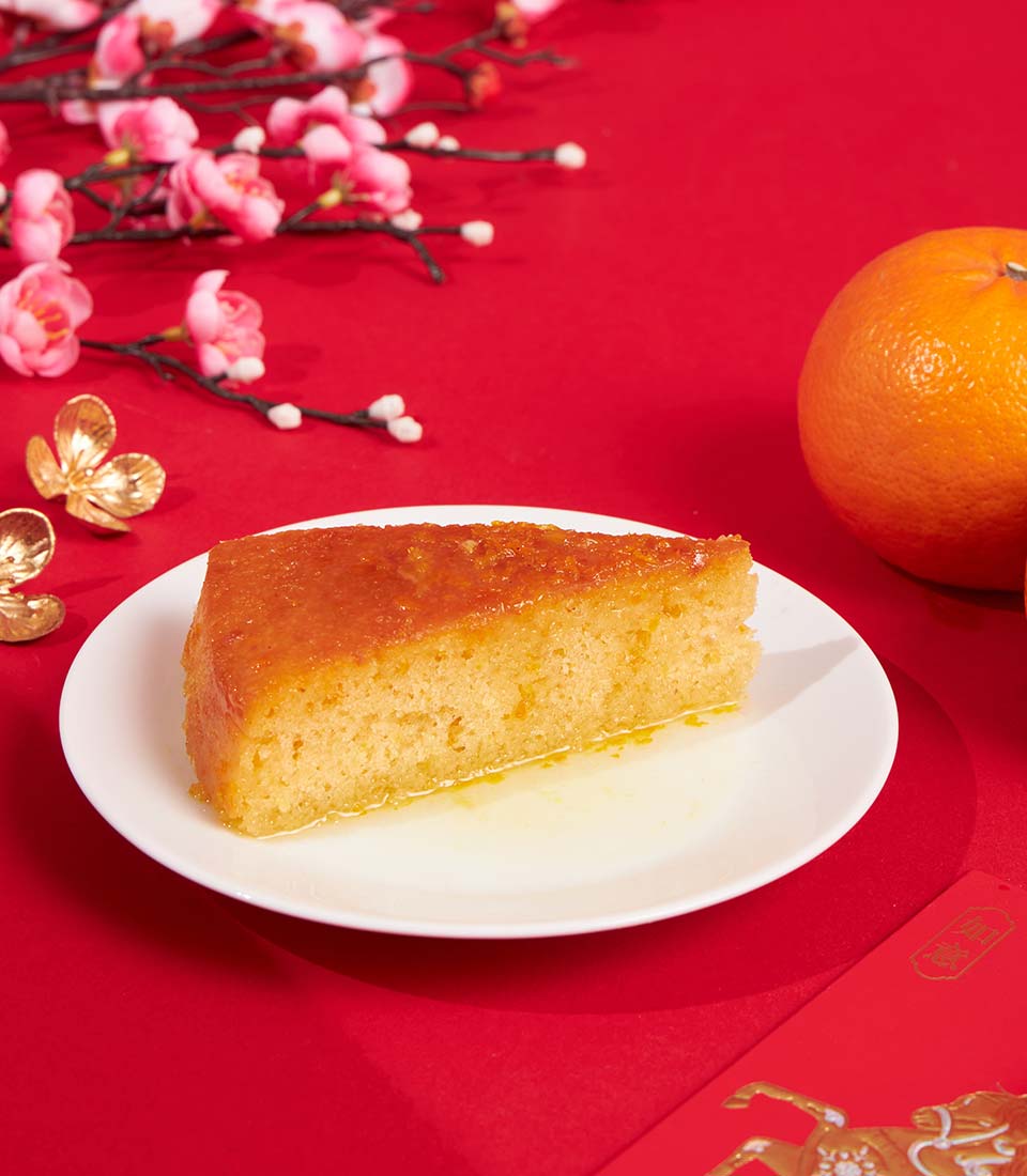 Golden mandarin orange sponge cake slice with glossy glaze, Chinese New Year gift hamper featuring cherry blossoms and red