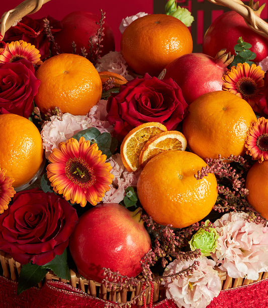 Vibrant Chinese New Year gift basket with fresh roses, mandarins, pomegranates, and gerbera daisies in woven wicker