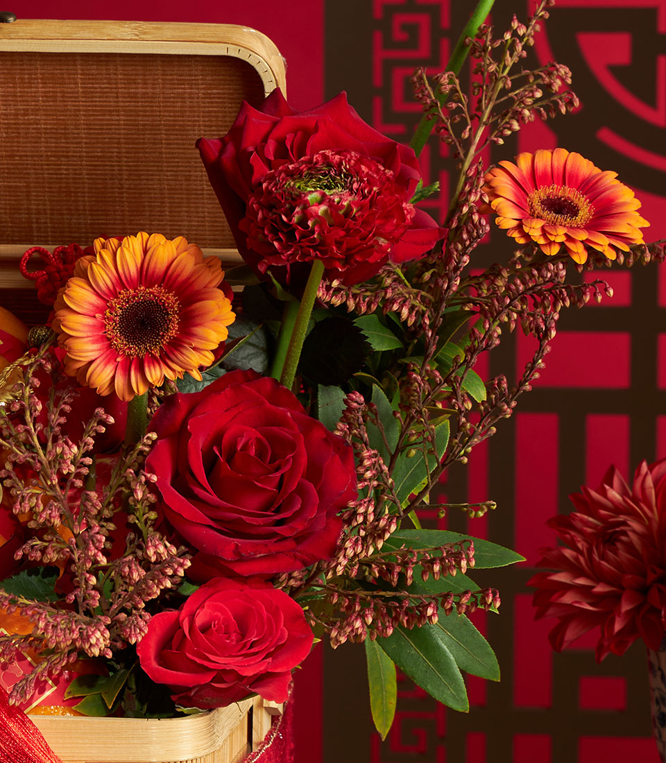 Red roses and orange gerberas with fresh berries in woven bamboo basket, Chinese New Year celebration arrangement