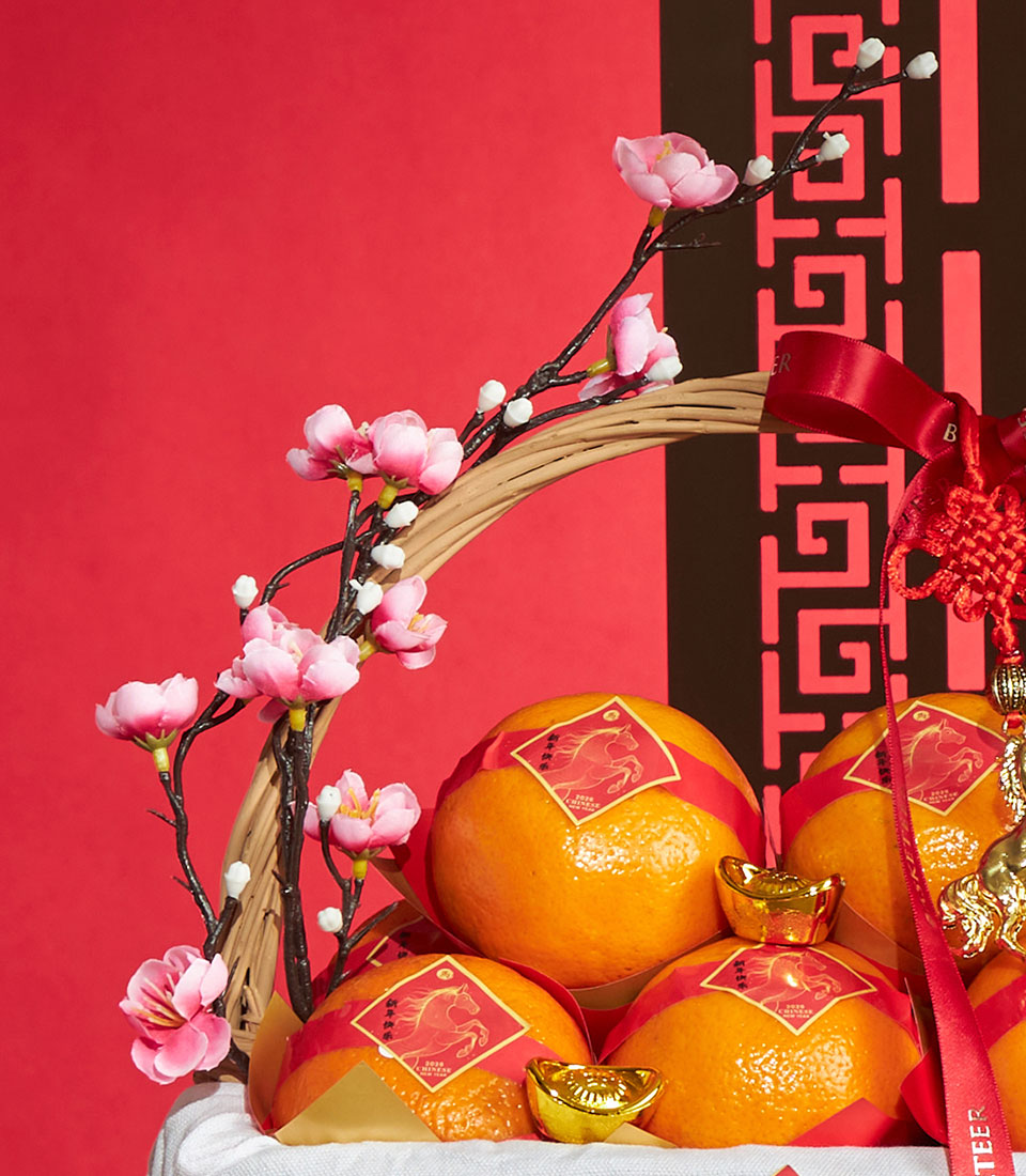 Festive Chinese New Year gift basket with mandarin oranges, gold ingots, cherry blossoms, and red silk ribbons