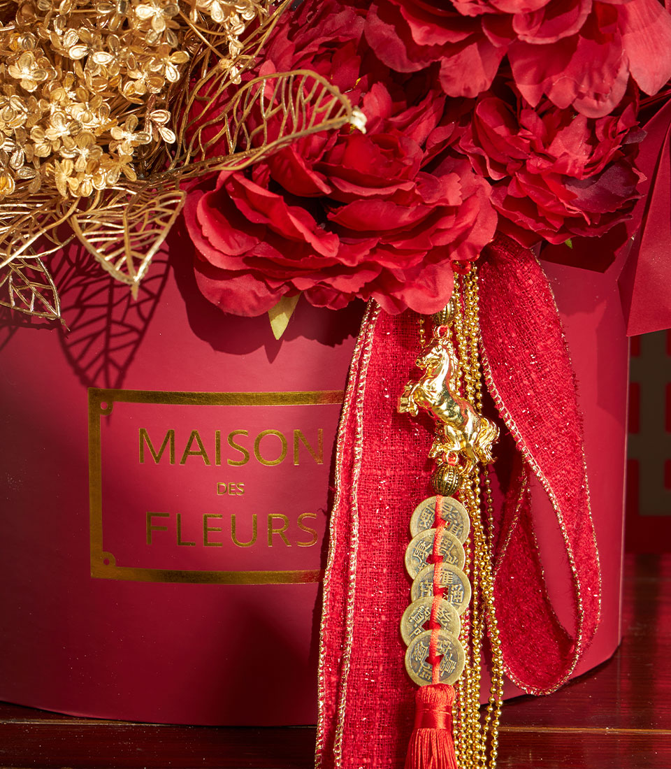 Basketeer luxury gift: Red floral arrangement with gold accents in round box. Red ribbon & horse charm. Premium hamper delivery Thailand for Chinese New Year.