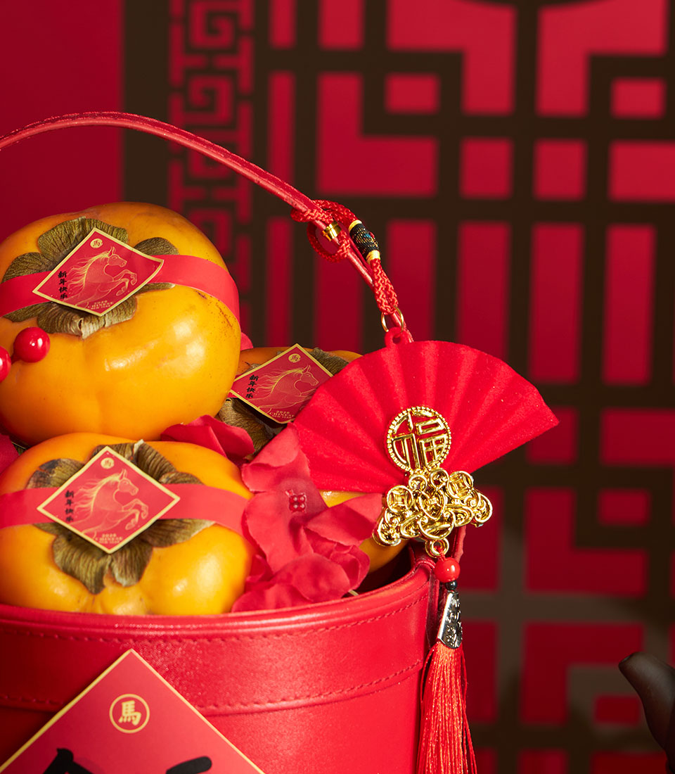 Festive Chinese New Year persimmon basket with red artificial flowers and golden lucky charms