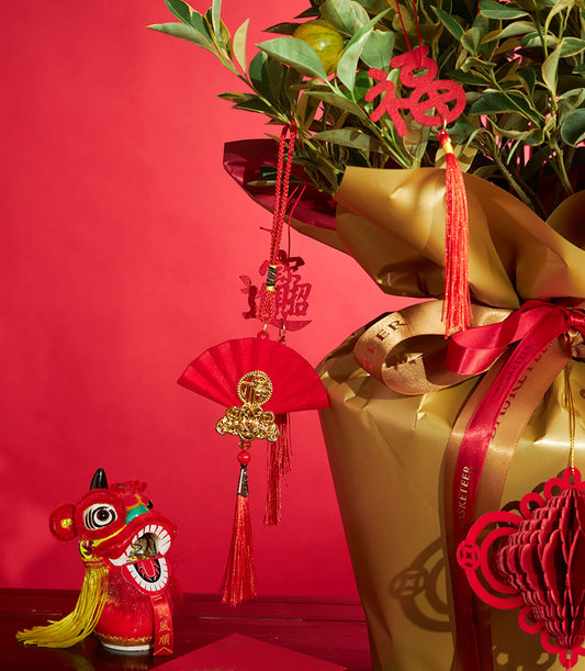 Variegated kumquat tree wrapped in gold with red prosperity charms, festive lantern and lion dance figurine for Chinese New