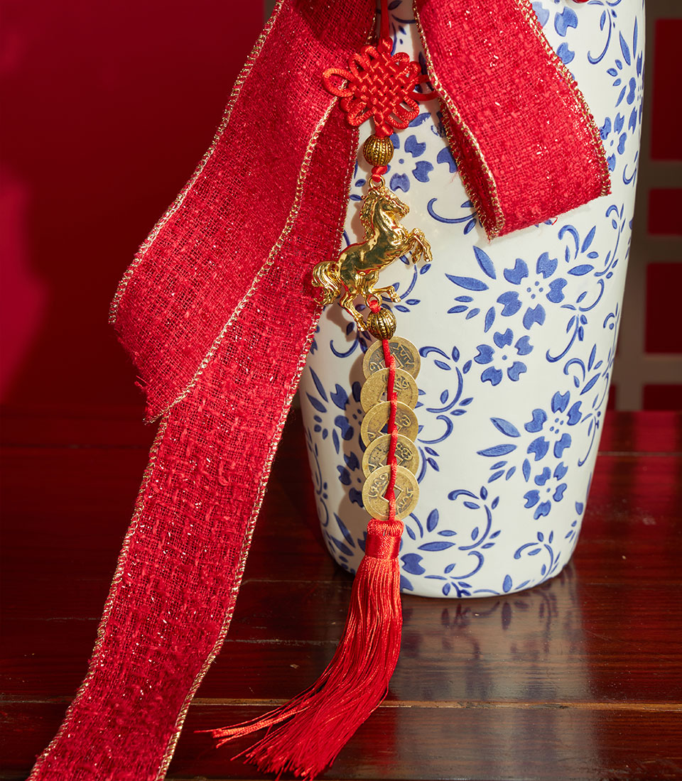Red amaryllis and berry branch arrangement in blue-patterned ceramic vase with Chinese knot charm and gold-edged ribbon