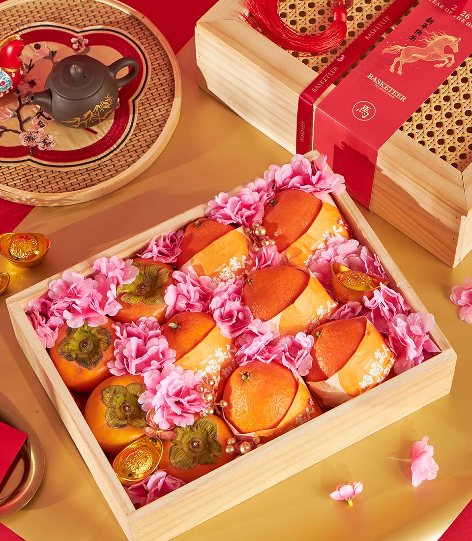 Festive Chinese New Year luxury fruit gift box with persimmons, tangerines, pink flowers, and golden accents in wooden crate