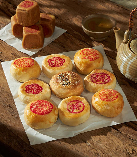 Golden Chinese pastries with red stamps and sesame seeds, paired with ceramic teapot and tea, for lunar new year gifting