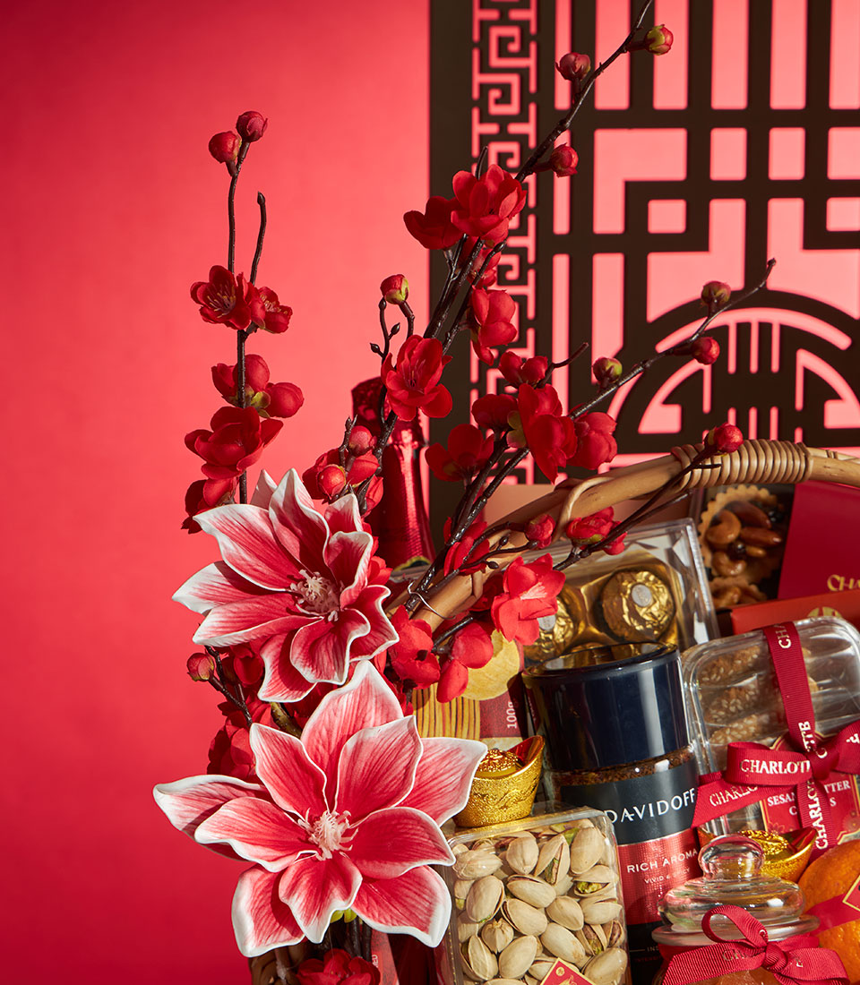 Festive red gift basket overflowing with gourmet treats, pistachios, premium coffee, gold chocolates, and cherry blossoms