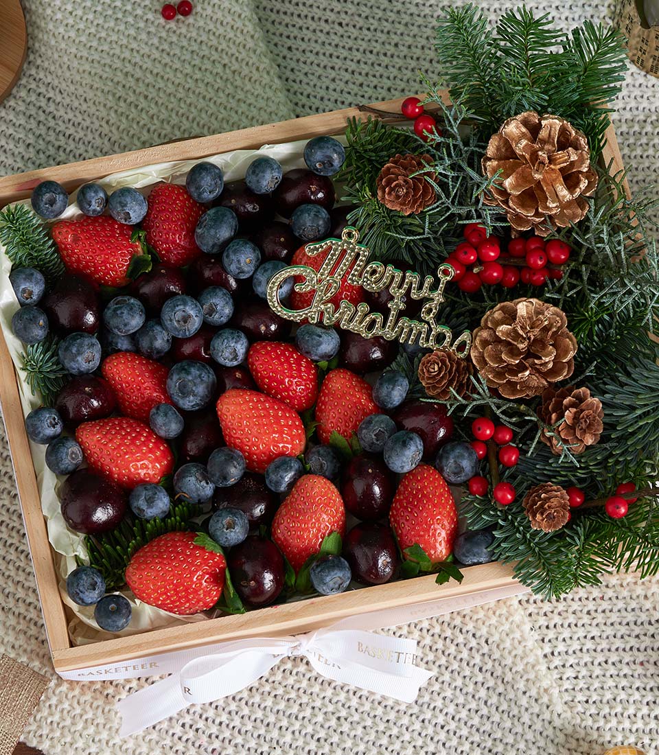 Festive wooden fruit box with strawberries, blueberries, cherries, and Christmas greenery decorated with gold accents