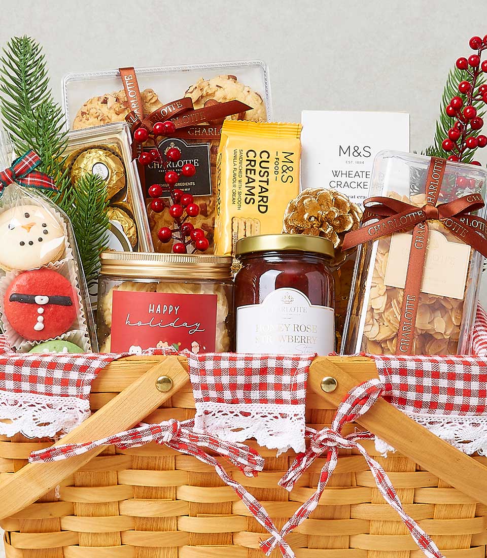 Festive Christmas gourmet snacks hamper with wicker basket, gingham ribbon, cookies, chocolates, and holiday greenery
