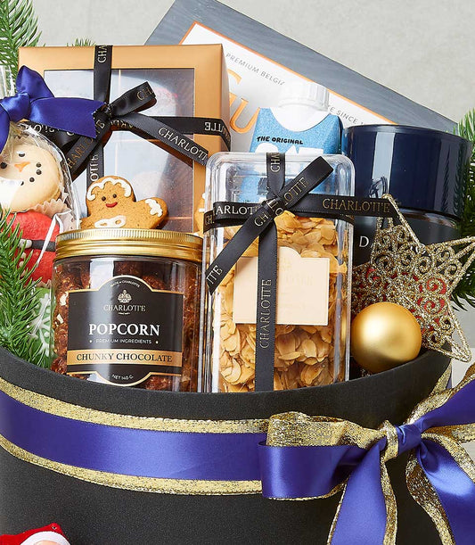 Festive gourmet gift hamper with chocolate popcorn, cookies, and holiday ornaments in black hatbox with blue ribbon