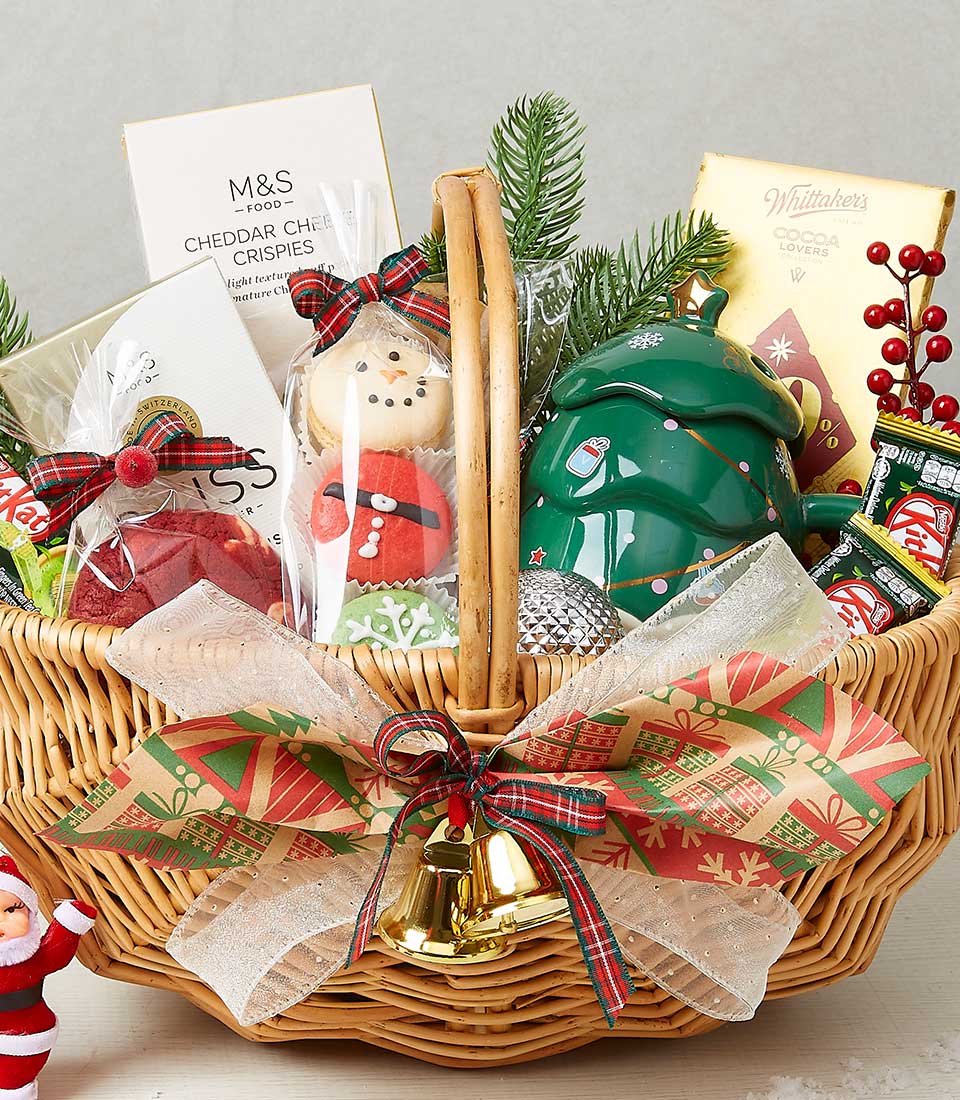 Wicker Christmas gift basket with holiday treats, festive mug, cookies, chocolates, and plaid ribbon with golden bells