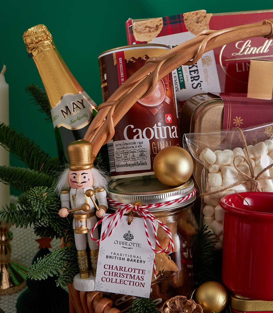 Festive Christmas gift basket with sparkling wine, chocolate, shortbread, and treats in woven basket with gold baubles and