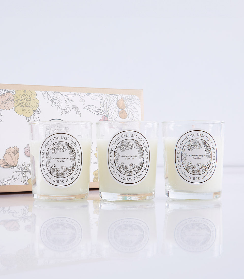 Three cream scented candles in glass votives with botanical labels, presented in luxury gift box