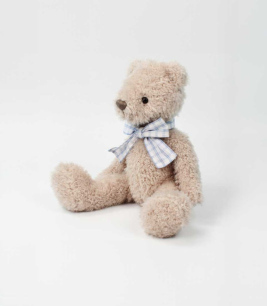 A tan, fluffy teddy bear with a blue plaid bow, ready to be included in a Basketeer premium hamper delivery in Thailand.