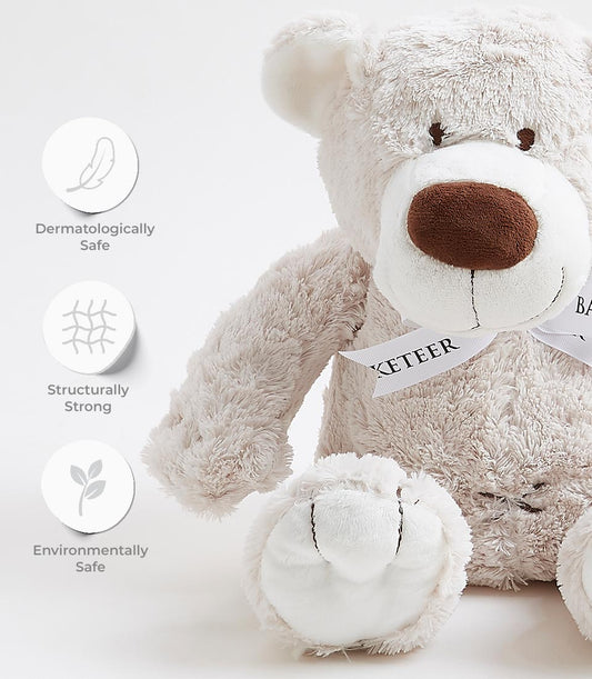 Soft beige plush teddy bear with brown nose, white ribbon collar, and safety certifications for babies and kids