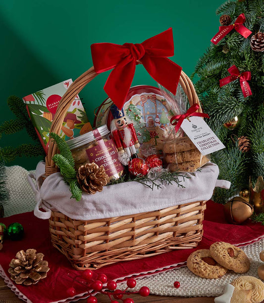 Festive Christmas gift basket with chocolate chip cookies, artisan chocolates, and baked goods in wicker with red velvet bow