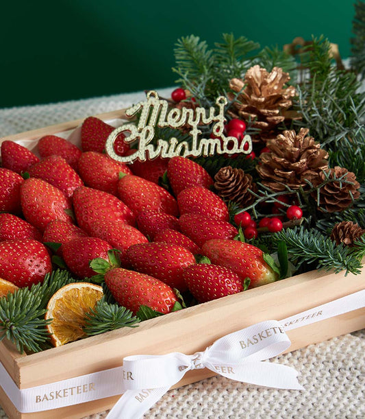 Premium fresh strawberries in wooden gift box with festive pine, pinecones, and gold Christmas ornament ribbon