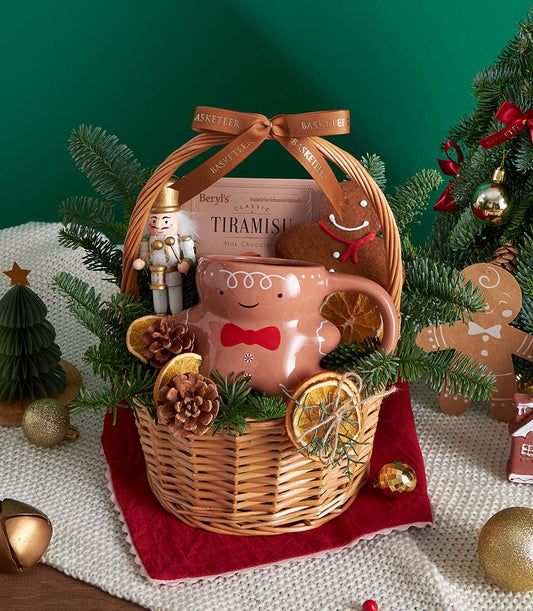 Festive wicker Christmas gift basket with gingerbread mug, tiramisu chocolate, and holiday decorations tied with brown ribbon
