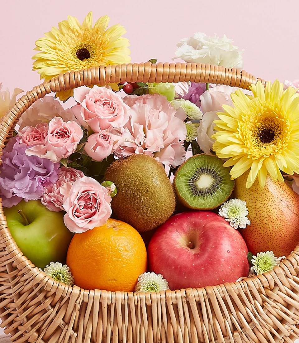 Wicker fruit basket with fresh apples, oranges, kiwi, pear, yellow gerberas, and pink roses for birthdays