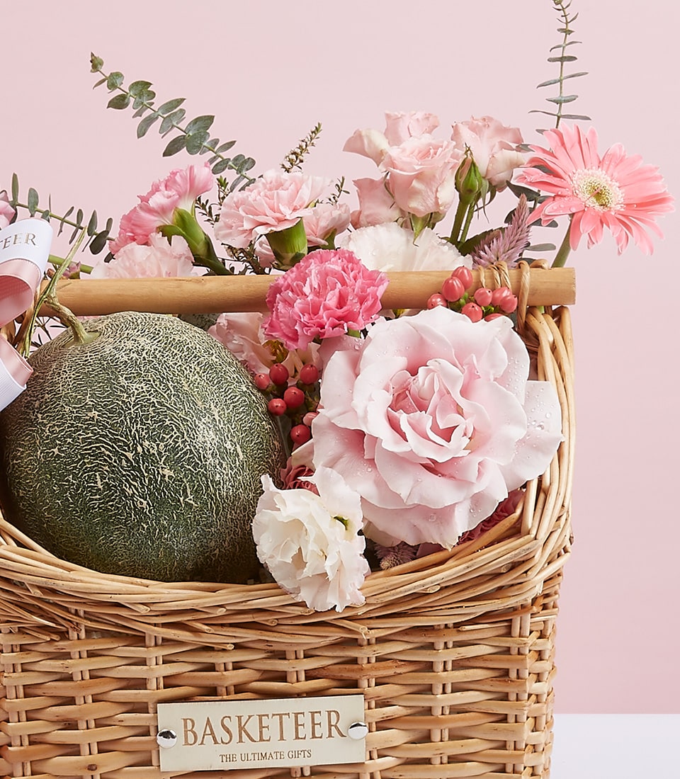 Wicker gift basket with fresh cantaloupe melon and pink rose, carnation, and gerbera daisy bouquet
