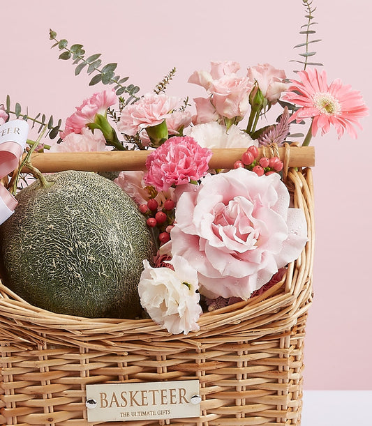 Wicker gift basket with fresh cantaloupe melon and pink rose, carnation, and gerbera daisy bouquet