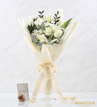 Elegant white roses, lilies, and daisies bouquet with cream paper wrap and satin ribbon in glass vase