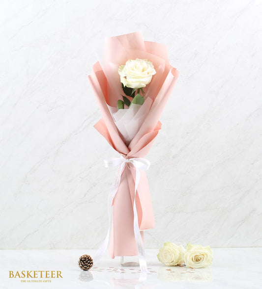 Elegant single white rose wrapped in blush paper with white ribbon, displayed in clear glass vase