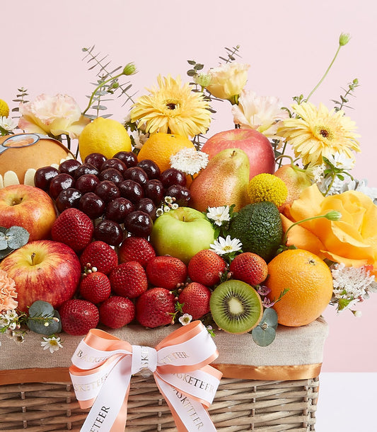 Vibrant mixed fruit gift basket with fresh apples, strawberries, citrus, and yellow gerbera daisies in woven wicker with