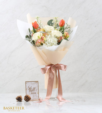 White and orange fresh flower bouquet with roses, hydrangeas, and tulips in rose-gold wrapped gift packaging