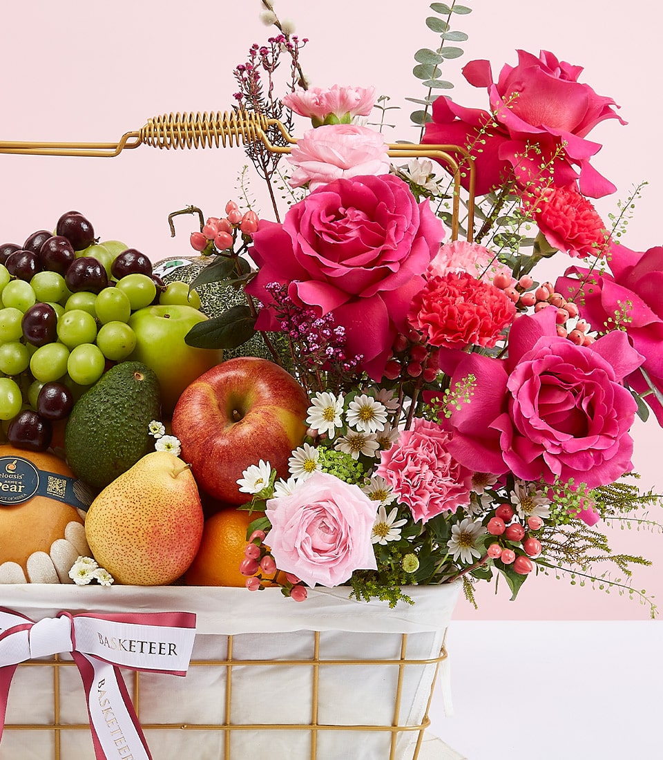 Premium mixed fruit basket with fuchsia roses, fresh grapes, apples, pears, and lush foliage in gold wire design