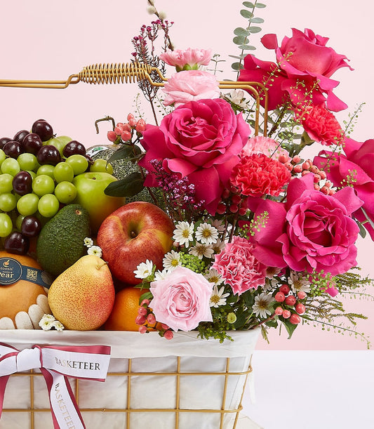 Premium mixed fruit basket with fuchsia roses, fresh grapes, apples, pears, and lush foliage in gold wire design