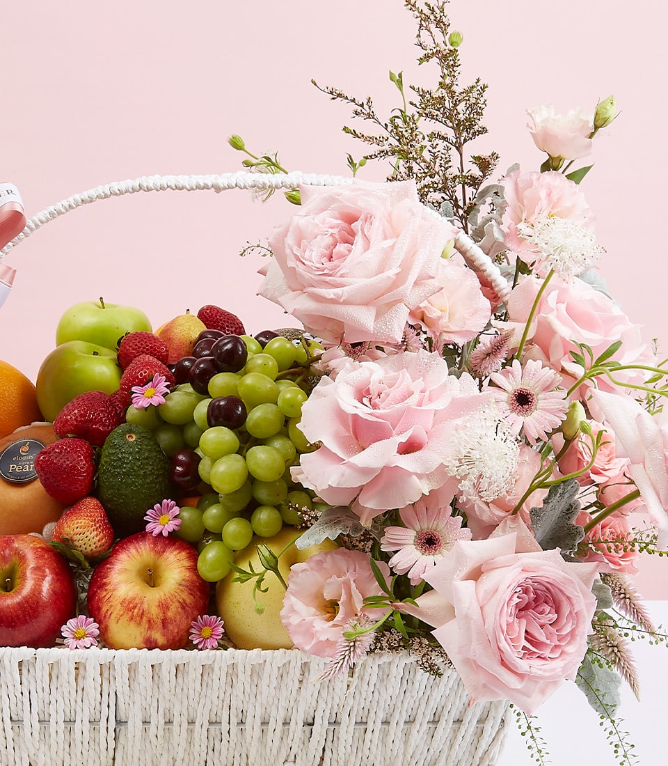 White woven basket with fresh fruit assortment and cascading pink roses, gerberas, and premium blooms