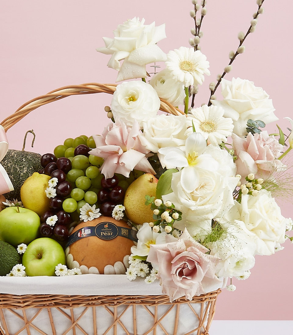 Premium fruit and flower gift basket with fresh grapes, apples, pears, and white roses in woven wicker
