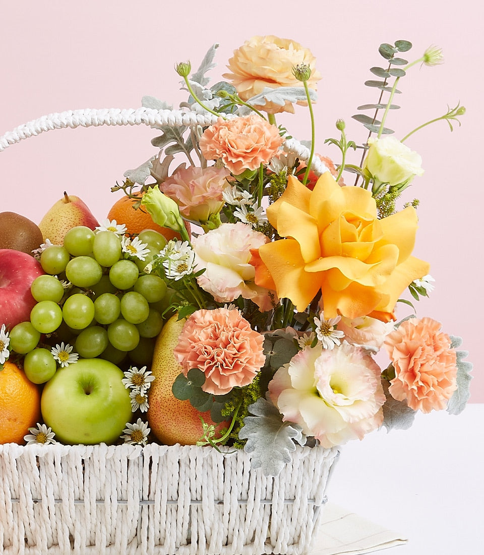 Sunny yellow roses and fresh fruit gift basket with apples, grapes, and tropical accents in white woven basket