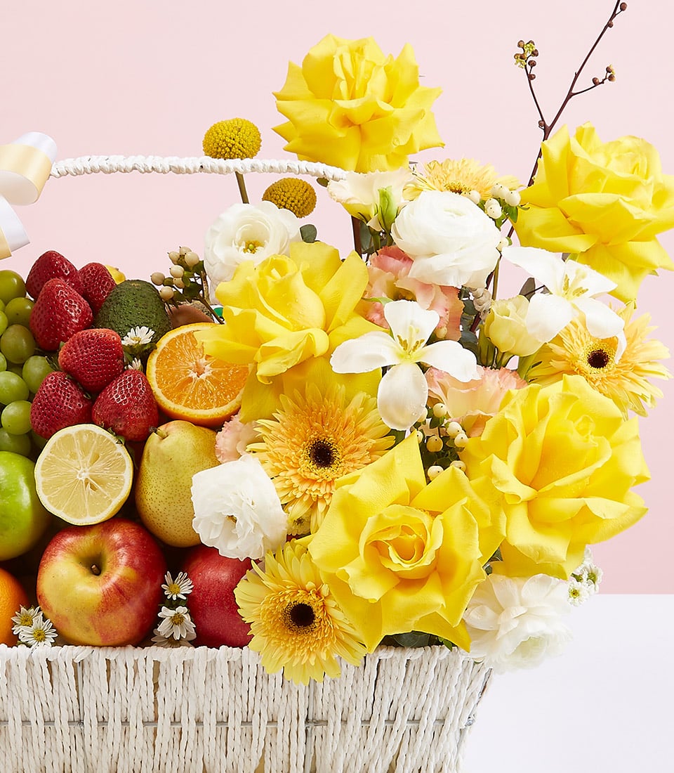 Premium white woven basket with fresh fruit medley and yellow roses, gerbera daisies, and white ranunculus