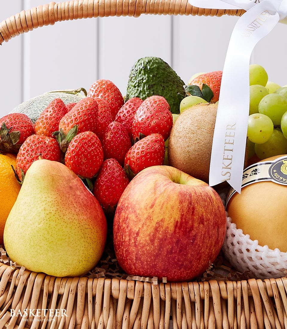Wicker fruit basket with fresh strawberries, avocado, cantaloupe, grapes, kiwi, apple, pear and orange, tied with satin