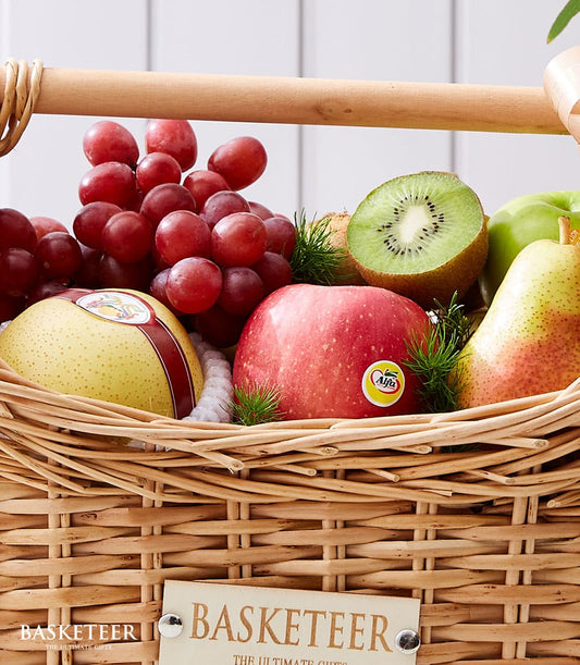 Woven wicker basket filled with fresh red grapes, pears, apples, kiwi, and green foliage
