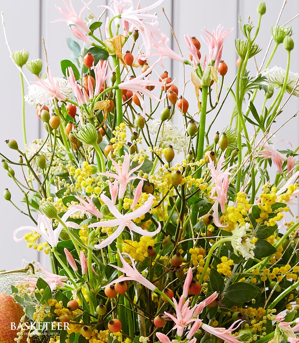 Vibrant mixed flower and berry arrangement with pink spider lilies, yellow mimosa, and orange rose hip clusters in lush,