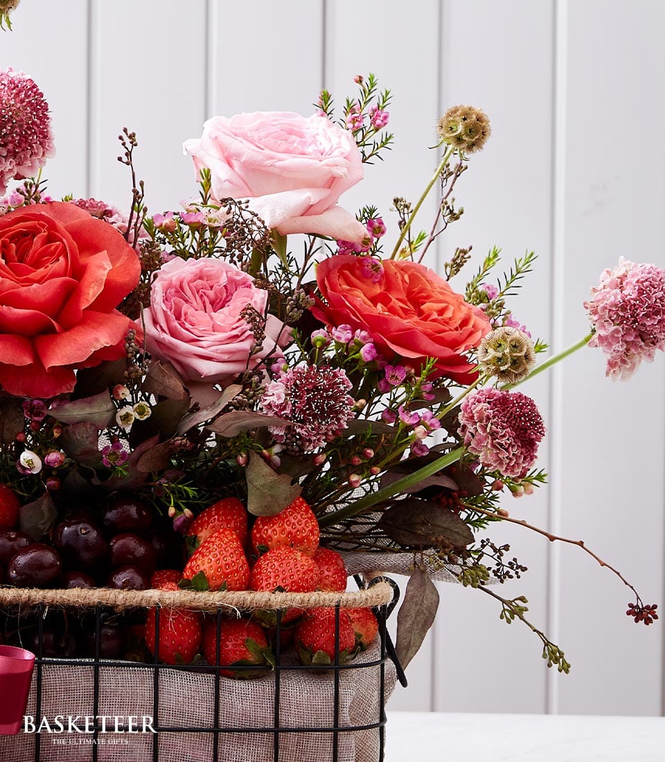 Vibrant pink and coral roses with fresh strawberries and grapes in black wire basket