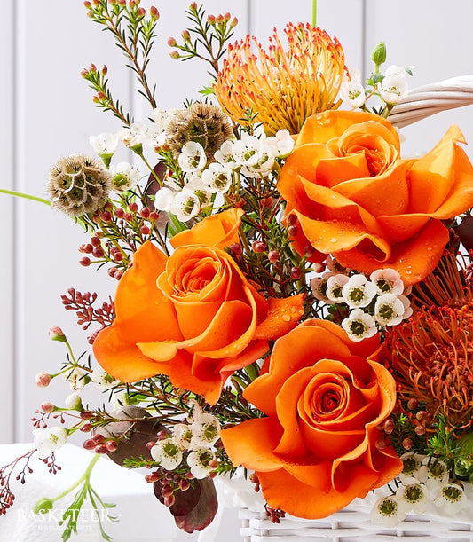 Fresh orange roses with tropical fruit flowers in white woven basket, congratulations gift arrangement