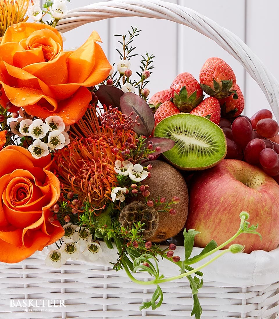 Vibrant orange roses and fresh fruit arrangement in white woven basket with strawberries, kiwi, and grapes