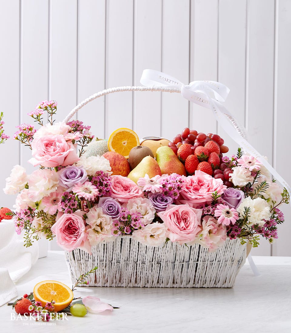 Luxury fruit and flower gift basket with fresh strawberries, grapes, citrus, and pink roses in woven white basket